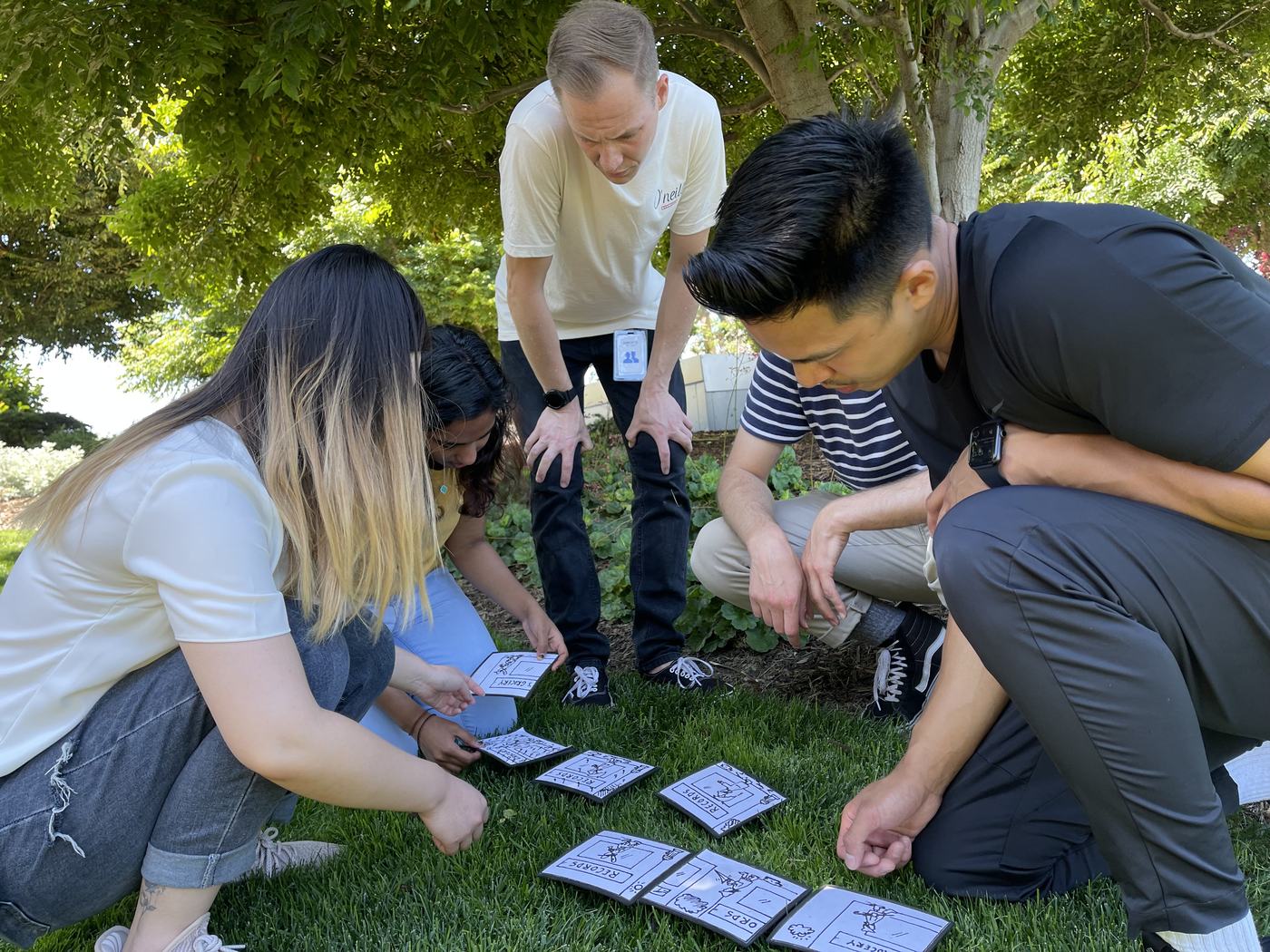 A team gathers closely around a tabletop puzzle outdoors